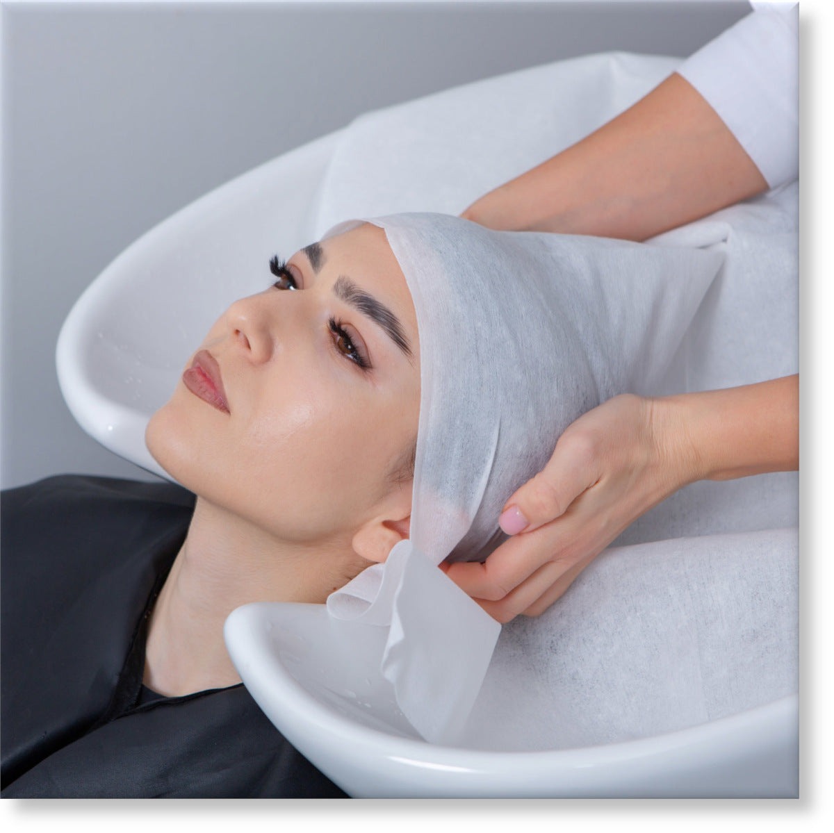 HairUncut | Tunika Disposable Salon Towels Image of a young woman reclining her head back about to have her hair wrapped in a disposable towel after washing her hair
